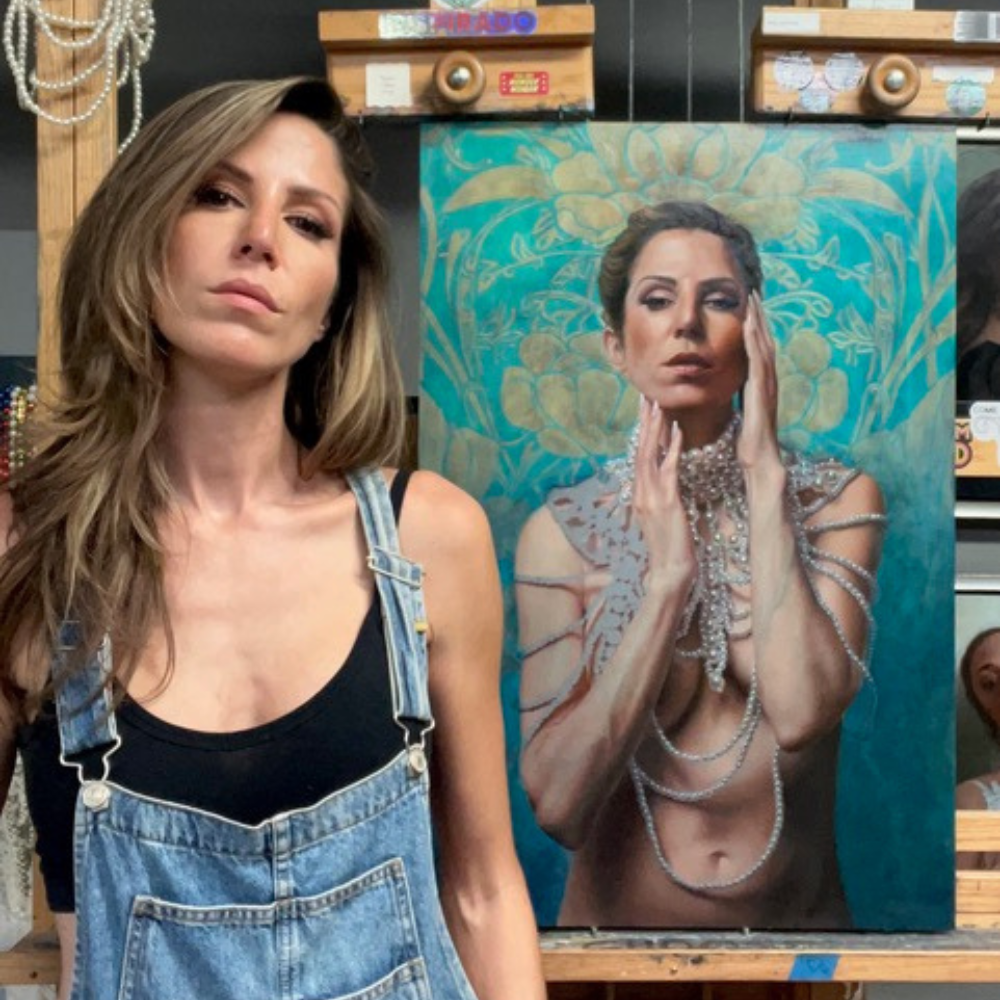 Shana Levenson in denim overalls standing with her ornate self-portrait painting highlighted by turquoise and pearl details.