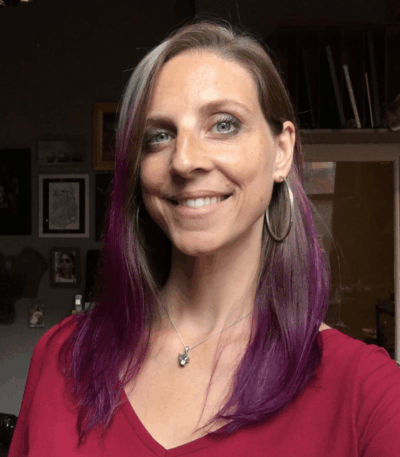 Julie Beck Workshop instructor smiling in studio headshot, purple-highlighted hair and hoop earrings, warm natural lighting.